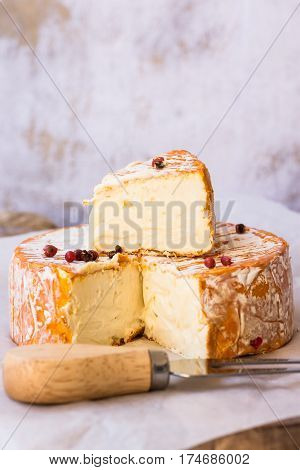 French German soft cheese with orange washed-rind fork red pepper corns cutting board concrete wall background