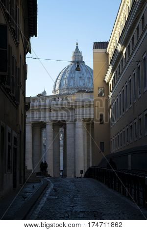 Saint Peter's dome in Rome seen through a typical roman alley