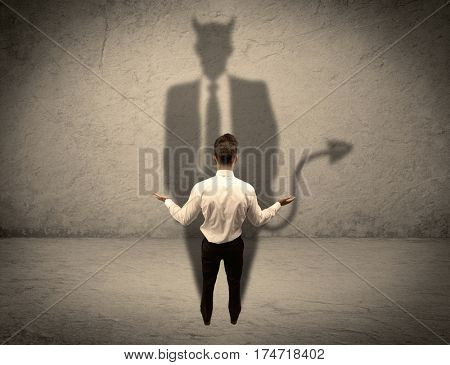 An experienced tricky businessman in suit looking at his devil desguise shadow reflected on the wall concept