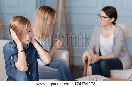 Bad words. Upset serious boy wearing jeans costume holding both hands on ears while looking straight