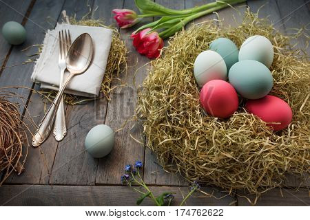 Decoration with colorful easter eggs in a nest and flowers on a old shabby wooden table