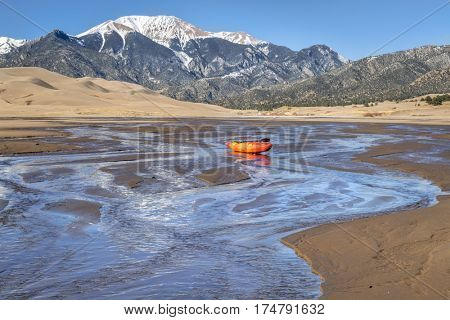 whitewater kayak in shallow waters of Medano Creek with Great Sand Dunes and Sangre de Cristo Mountains in background