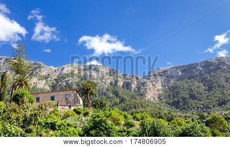 Traditional stone house with garden in mountain village Deia, Majorca island, Spain. View to the mountain peaks of Serra Tramuntana.