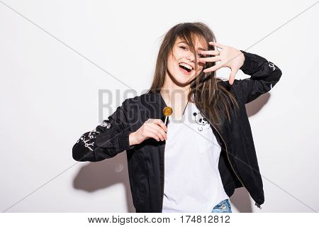 Young girl eating chupa chups over grey background.