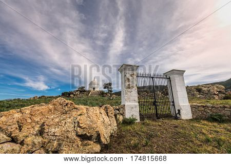 Wispy clouds above large iron gates and painted stone pillars leading to the steps to a large white domed mausoleum at Palasca in the Balagne region of Corsica