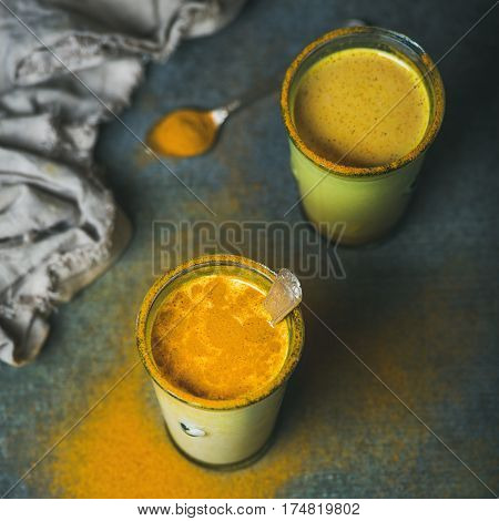 Golden milk with turmeric powder in glasses over dark grunge background, square crop, copy space. Health and energy boosting, flu remedy, natural cold fighting drink. Clean eating, weight loss concept