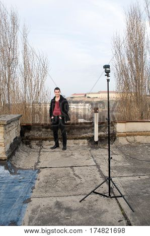 Photographing smiling Danila Mazić in a tight red shirt unbuttoned covered with a black coat and black pants a background Petrovaradin fortress and the Danube River, Novi Sad, Serbia