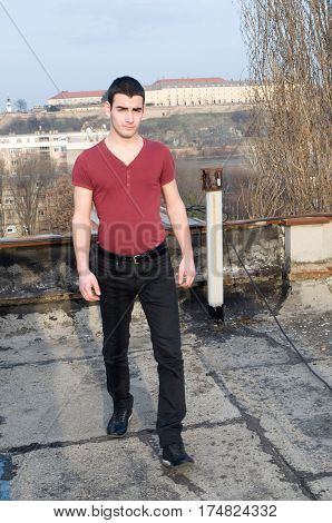Photographing Danila Mazić in a tight red shirt and black pants with their hands beside the body a background Petrovaradin fortress and the Danube River, Novi Sad, Serbia