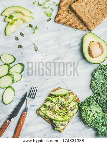Healthy green veggie breakfast. Sandwich with avocado, cucumber, kale, kress sprouts, pumpkin seeds over marble background, top view, copy space. Vegan, weight loss, clean eating, detox food concept