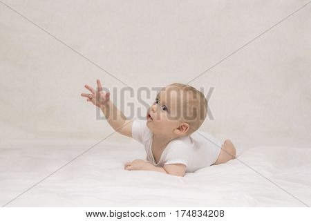 Adorable 8-month infant kid lying on the bed and holdes out his hand. Hotizontal studio shot. Copy space