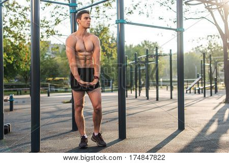Fitnes man posing on street fitness station showing his muscular body Full lenght portrait