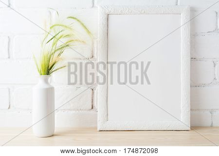 White frame mockup with golden yellow and green wild grass ears in styled vase near painted brick wall. Empty frame mock up for presentation design. Template framing for modern art.