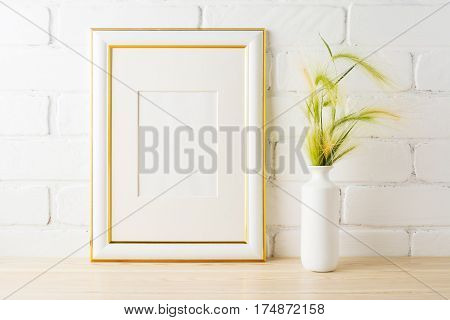 Gold decorated frame mockup with yellow and green wild grass ears in styled vase near painted brick wall. Empty frame mock up for presentation design. Template framing for modern art.