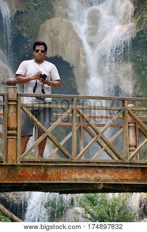 People travel and stand on the bridge looking and take photo viewpoint of Kuang Si Falls or Tat Kuang Si Waterfalls in Luang Prabang Laos