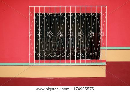 Black window with fancy white security grill in colorfully painted wall (red, cream, pink) in Puerto Ayora, Galapagos Islands, Ecuador