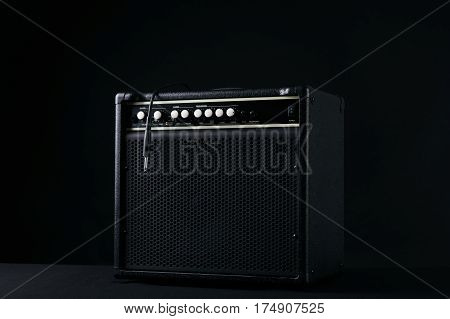 Black guitar amplifier with jack cable on black background.