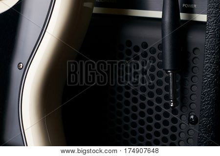 Black and white electric bass guitar with jack cable and classic amplifier on a dark background.Close up.