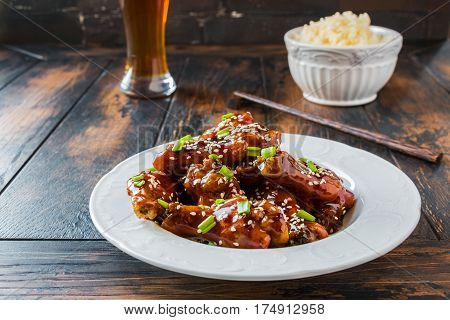 Crispy sesame chicken wings with a sticky sweet Asian sauce and white boiled rice on a plate on wooden table.
