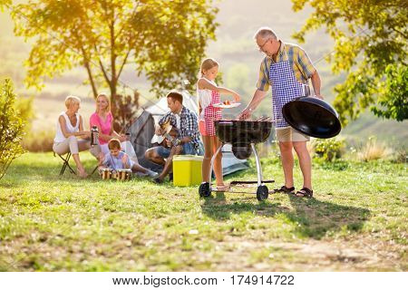 Grandfather and granddaughter at barbecue grill with family having diner