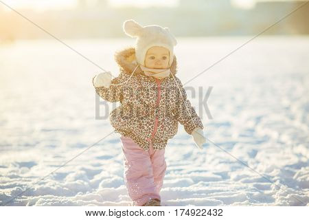 little girl walks through the snow in a warm jaket and hat