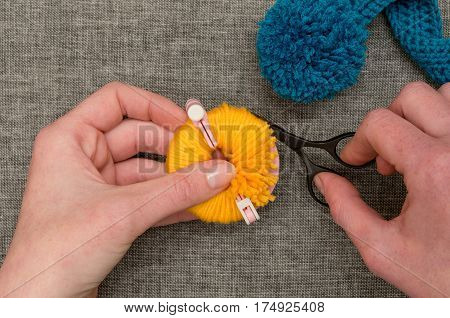 Hands Cutting Yellow Yarn Wrapped Around Pom-pom Maker