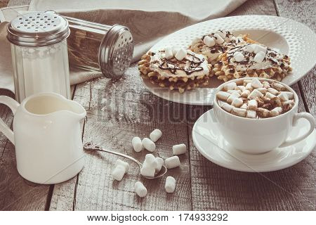 White cup of coffee with milk marshmallow and homemade waffle with whipped cream with decor on top. Tasty breakfast. Vintage toned.