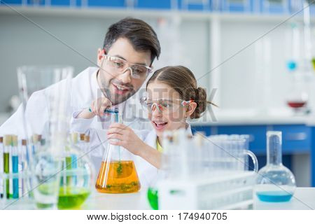 Man teacher and girl student scientists in protective glasses making experiment in lab