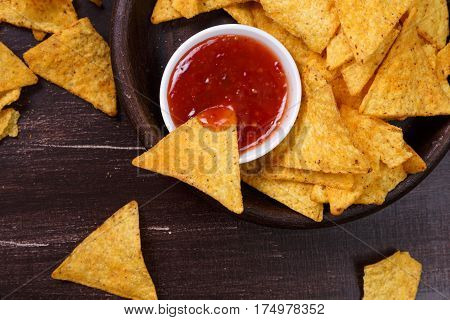 Nachos chips. Delicious salty tortilla with sweet salsa or chilli sauce. Snack on rustic plate. Sackcloth on wooden background.