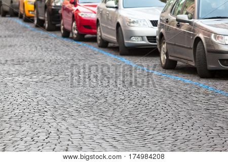 Cobblestone road with row of colorful cars at parking zone on the street behind a blue diagonal line (copy space)