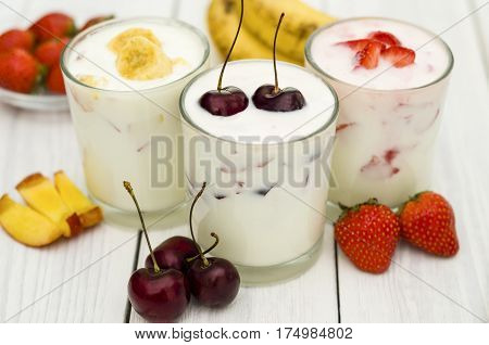Strawberry, banana and cherry yoghurt on a white wooden background. Healthy diet