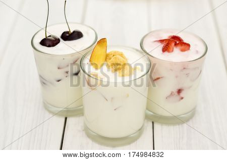 Strawberry, banana and cherry yoghurt on a white wooden background. Healthy diet