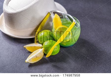 colored drink a combination of blue and green decorated with lemon and melon a glass a piece of lemon and two limes yellow sunglasses white hat party set