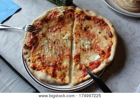 Cut in two halves pizza with cutlery on served restaurant table. Cut pizza serving with fork and knife on white tablecloth in cafe.