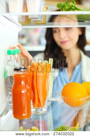 Portrait Of Female Standing Near Open Fridge Full Of Healthy Food, Vegetables And Fruits. Portrait O