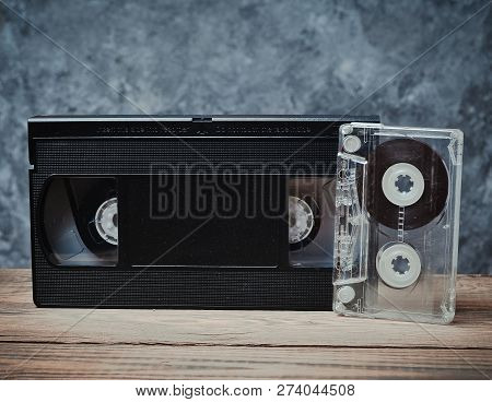 Audio And Video Cassette Close-up On A Wooden Shelf Against A Gray Concrete Wall. Retro Technology F