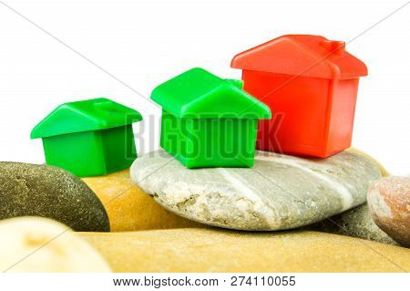 Three Little Green And Red Houses Made Of Plastic Are Laying On Bunch Of Grey Pebblestones