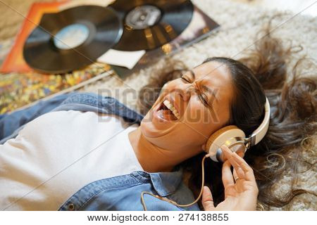 Vibrant young brunette listening to vinyl records with heaphones