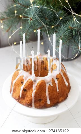 Pie With Raisins And Icing From Powdered Sugar On The Background Of Fir Branches And Garlands. Rusti