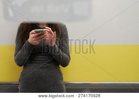 A Girl With A Smartphone Is Standing Behind A Glass Door. A Sign On The Door Covers The Girl's Face