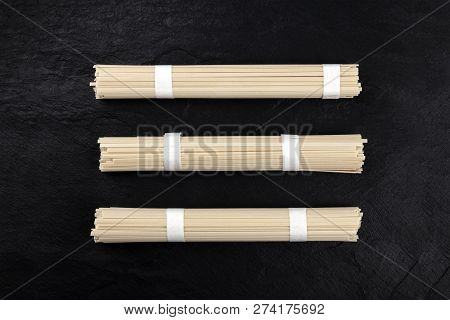 Three Individually Wrapped Portions Of Udon Noodles, Shot From The Top On A Black Background With A 