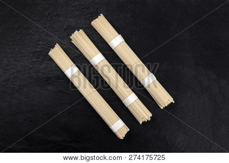 A Photo Of Three Individually Wrapped Portions Of Udon Noodles, Shot From The Top On A Black Backgro