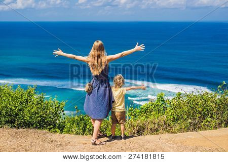 Mom And Son Travelers On A Cliff Above The Beach. Empty Paradise Beach, Blue Sea Waves In Bali Islan