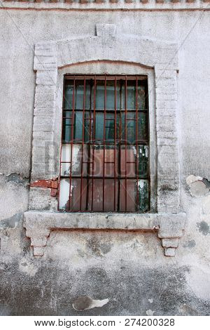 Old Window With Iron Bars. Wooden Window With Dirty Glasses And Antique Rusty Grate With A Torn Net.