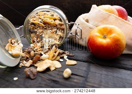Homemade Granola In Glass Jar And Apples In Reusable Fabric Bag On Dark Wooden Table With Texture. H