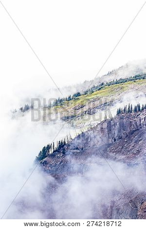 Huge Harsh Purple Mountainrange With Green Trees And Clouds Cover