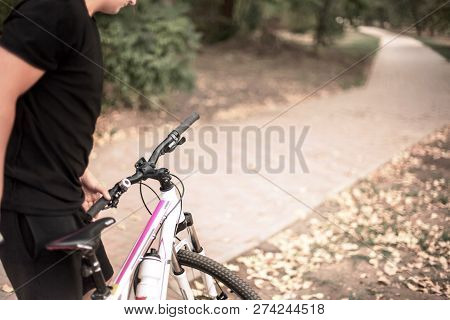 Young Caucasian Man Holding The Pink-and-white Bicycle In Front Of Abandoned Path In The Park, Weari