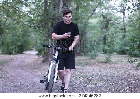 Young Handsome Caucasian Man With Dark Hair Using Mobile Phone, With Bicycle In The Abandoned Melanc
