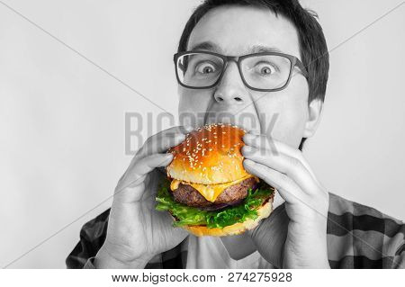 A Young Guy With Glasses Holding A Fresh Burger. A Very Hungry Student Eats Fast Food. The Concept O