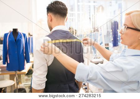Side View Portrait Of Tailor Measuring Back Of Mature Bearded Man Fitting Bespoke Suit In Traditiona