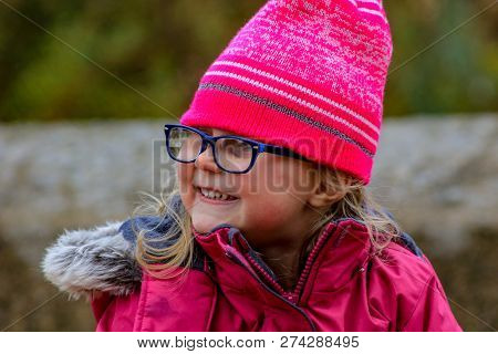 Closeup Half-turned Portrait Of Little Girl In Grey Jacket With Fur Collar And Knitted Hat In Snowy 